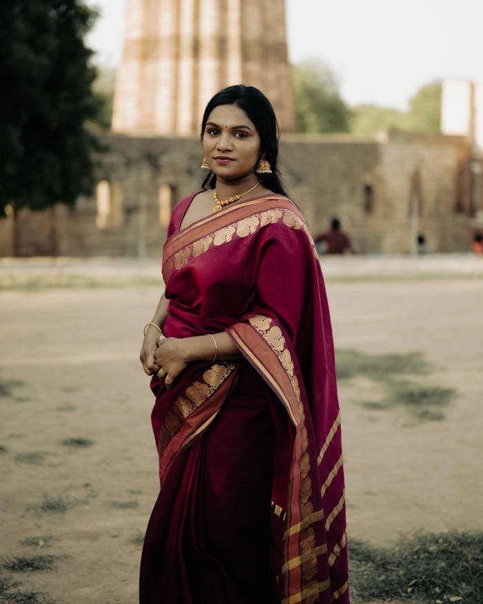 Indian woman in traditional saree posing outdoors with architectural background.