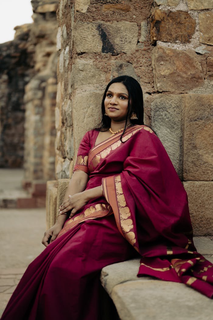 Portrait of a woman in a vibrant sari posed against an ancient stone wall, exuding traditional elegance.