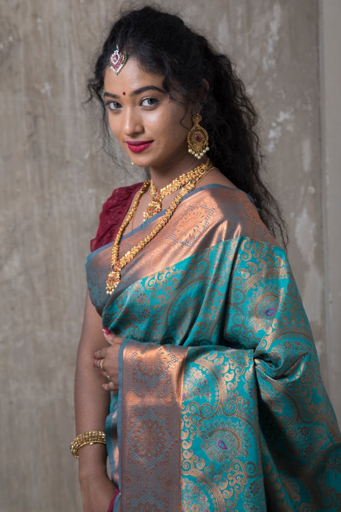 A woman in a traditional saree with gold jewelry posing gracefully indoors.