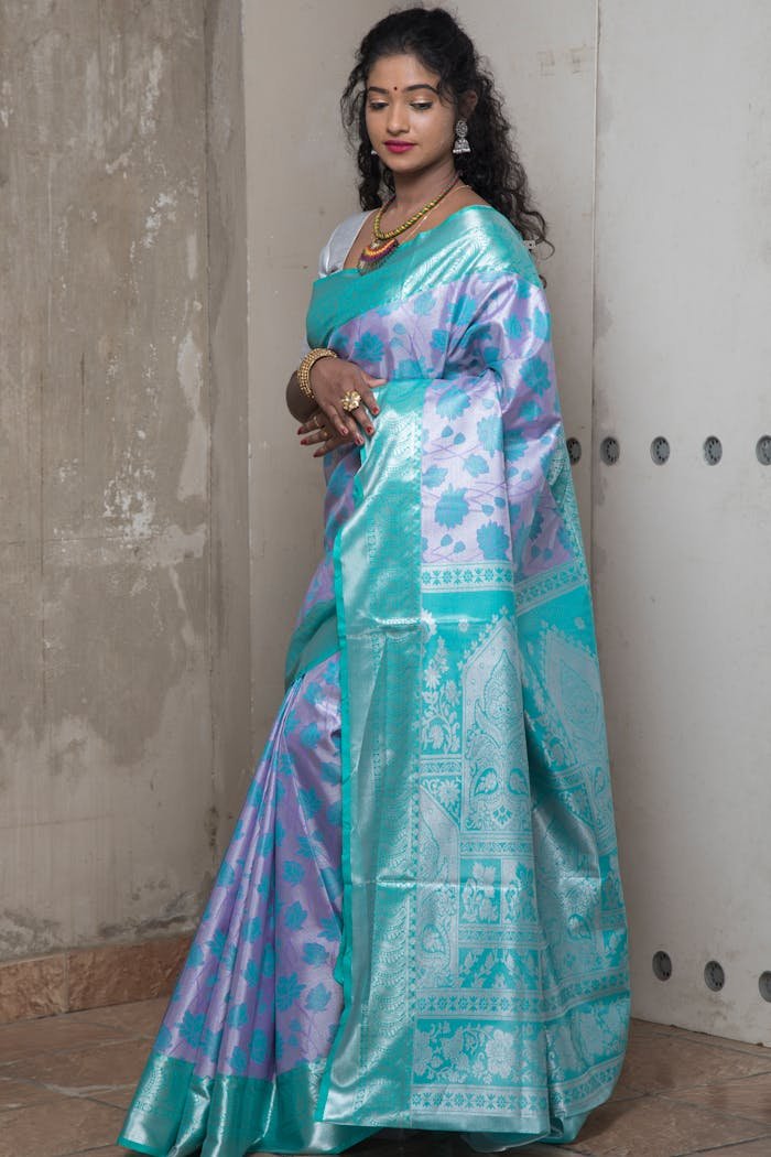 Graceful woman in traditional teal and purple saree poses elegantly indoors.