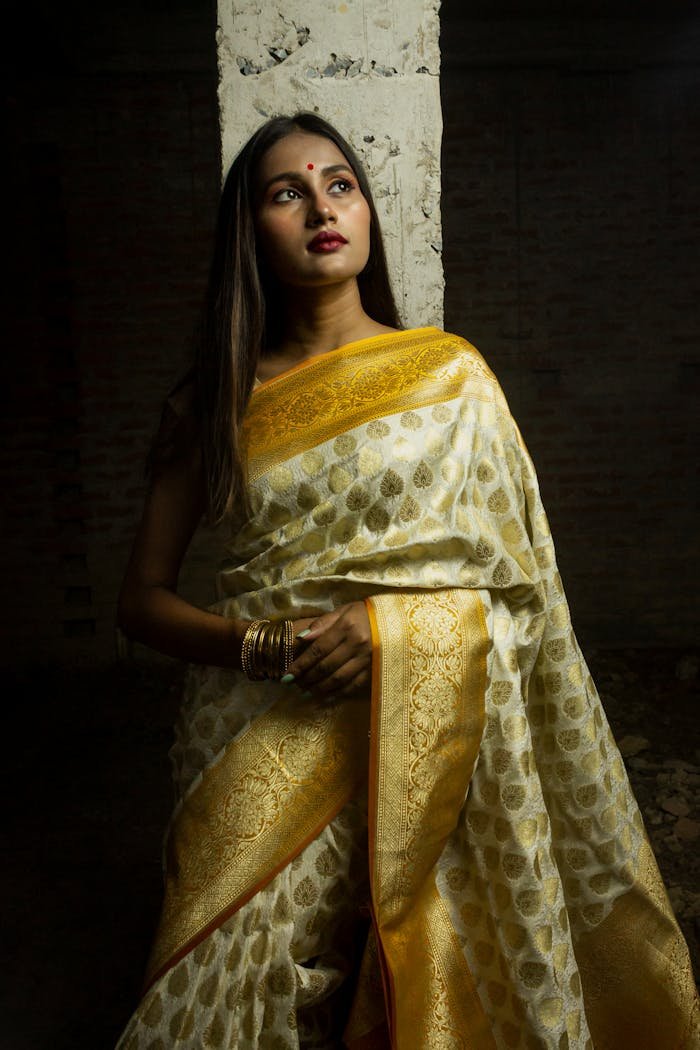 Portrait of a South Asian woman in a traditional yellow and gold sari, posing against a textured backdrop.